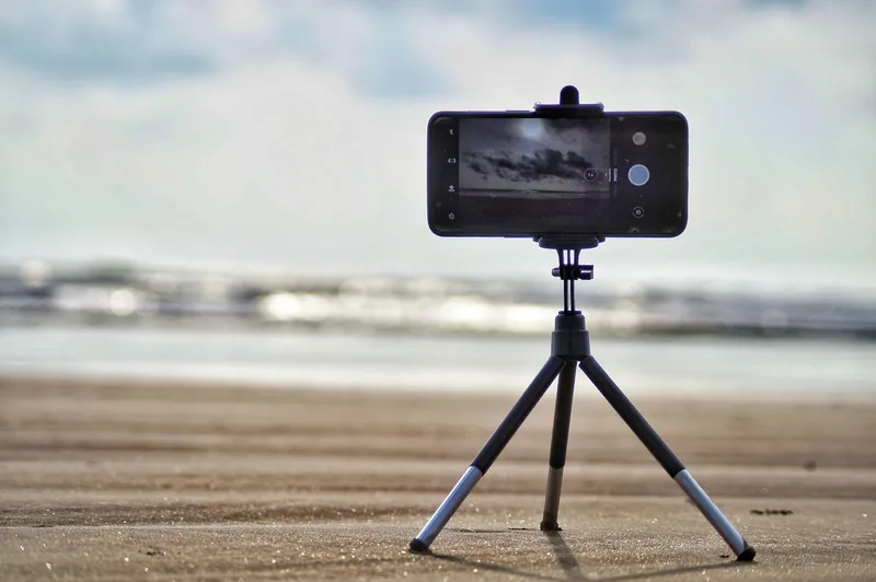 三脚に固定されたスマートフォンが、砂浜を向いて置かれている写真