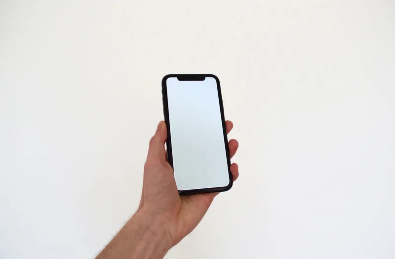 白い背景の前で、スマートフォンを片手で持っている写真